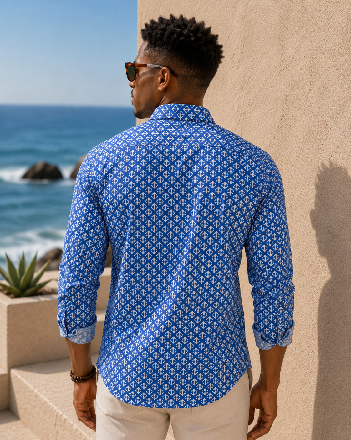 Man wearing a blue patterned shirt standing by a coastal building.