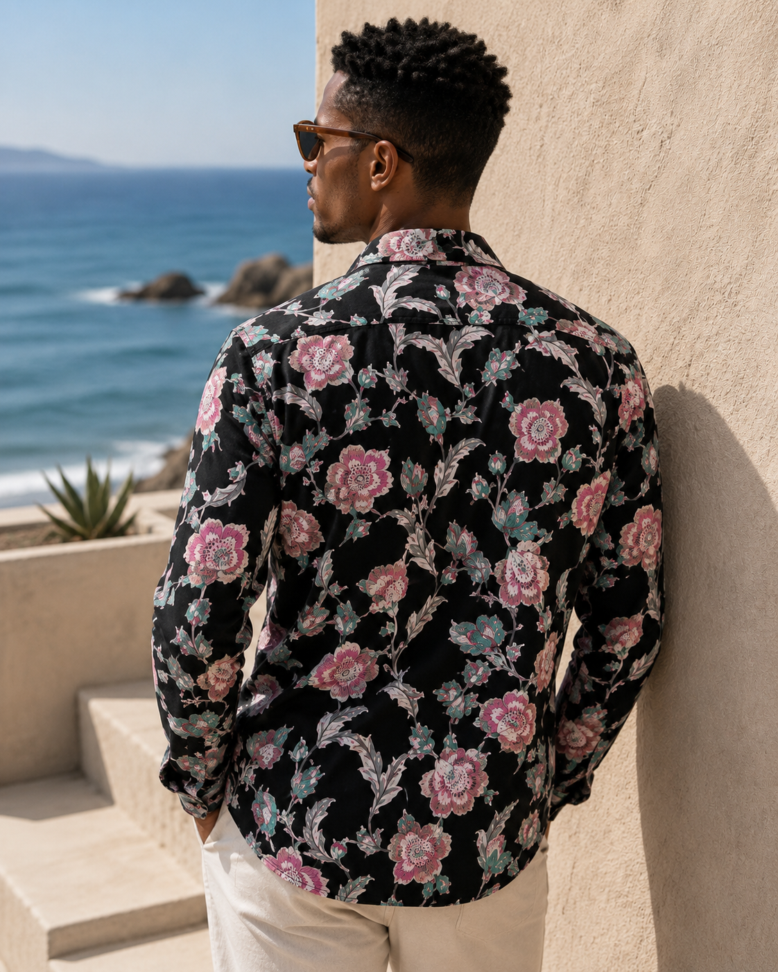 Man wearing a floral shirt leaning against a wall with ocean view