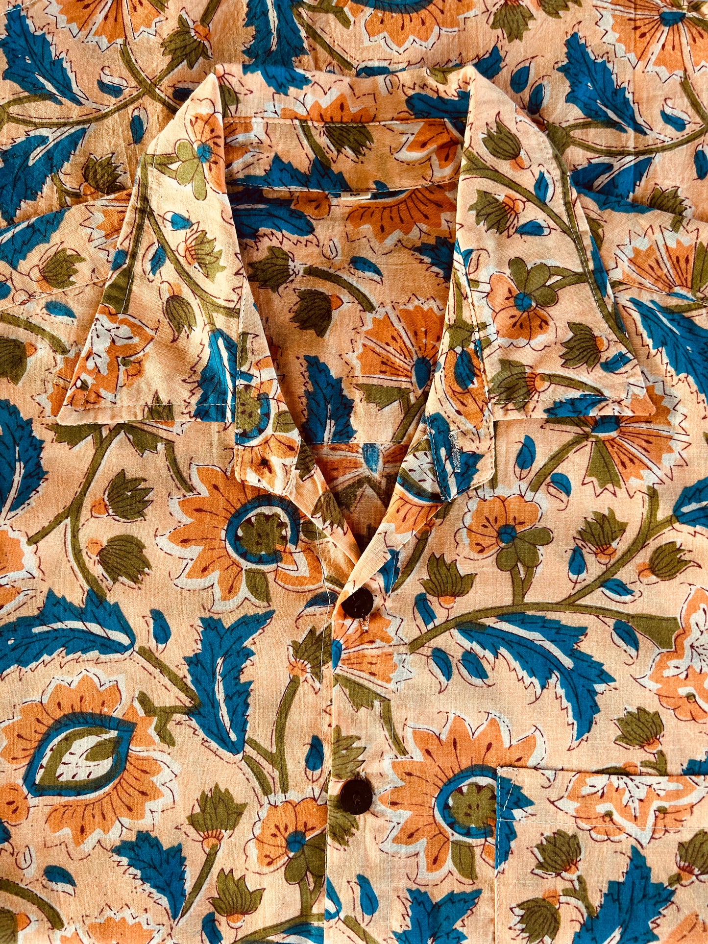 Close-up of a fabric with a floral pattern featuring orange, blue, and green colors on a beige background.