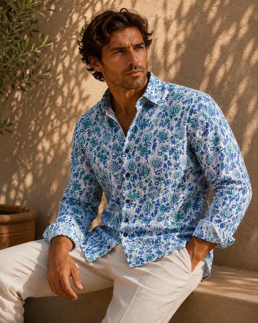 Man wearing a blue floral shirt sitting against a beige wall.