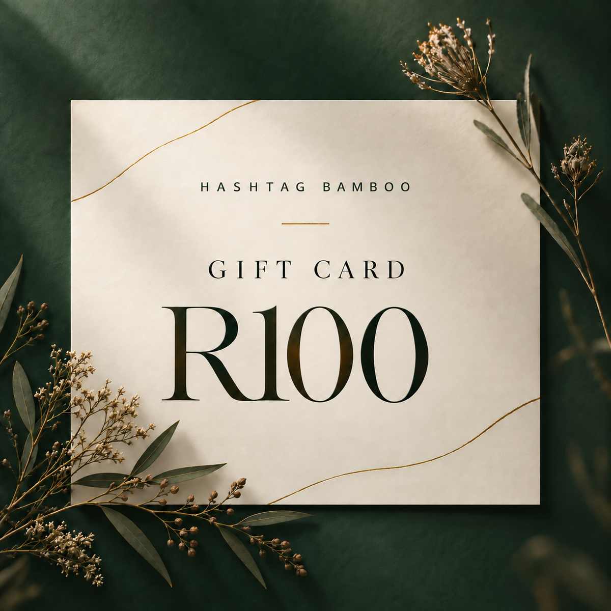 A square cream gift card with elegant typography reading 'HASHTAG BAMBOO GIFT CARD R100' in dark green and gold, styled on a dark green background with dried botanical sprigs.