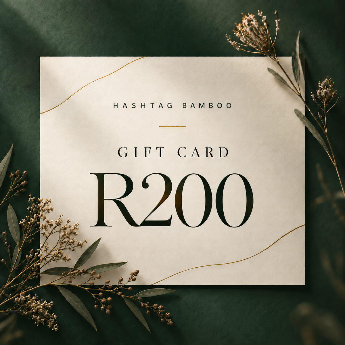 A square gift card reading 'HASHTAG BAMBOO GIFT CARD R200' in dark lettering on a warm off-white card, styled on a deep green background with dried botanical sprigs and thin gold lines.