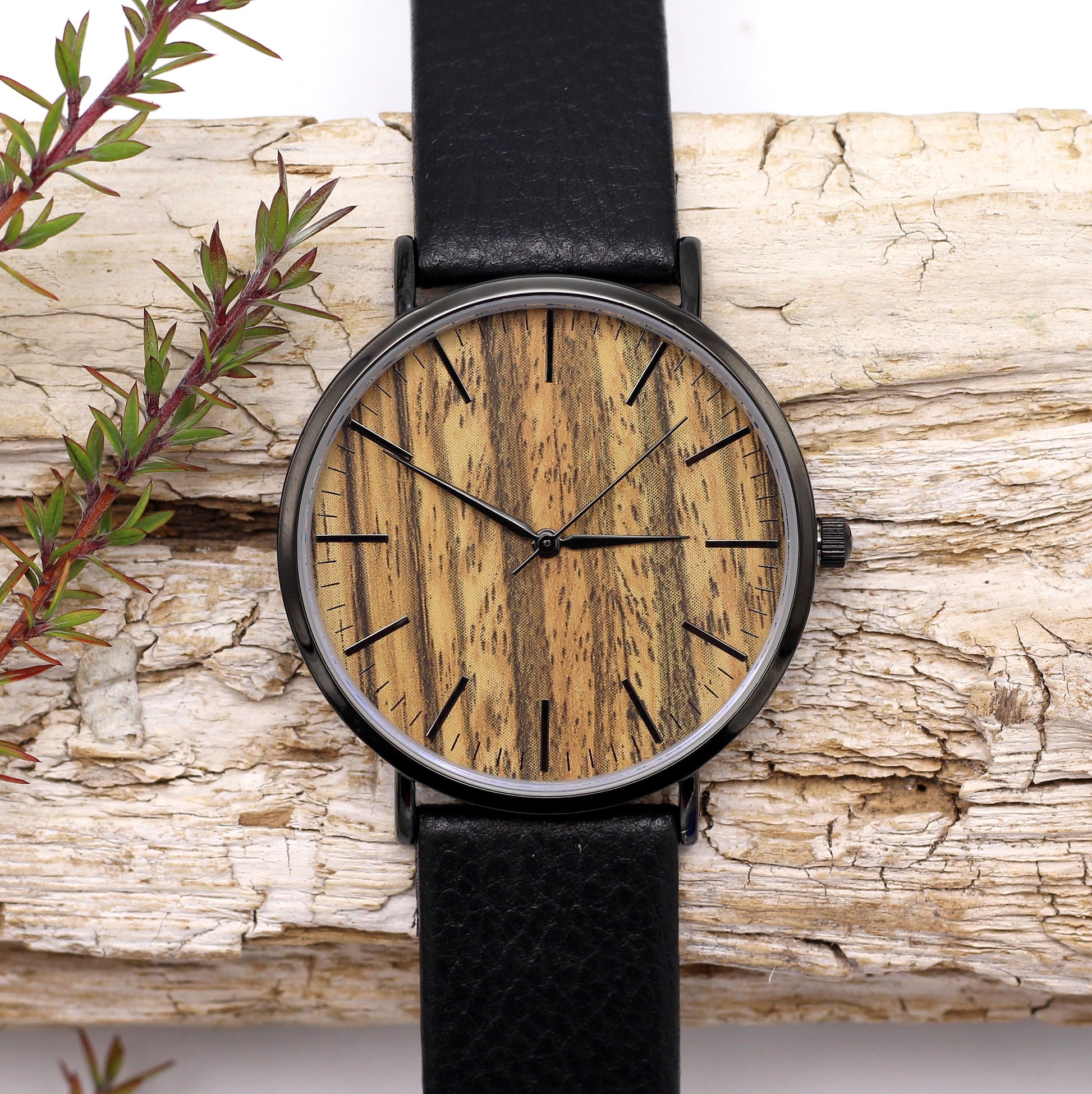 A sleek black stainless steel and wood watch with a leather strap displayed on a wooden surface.