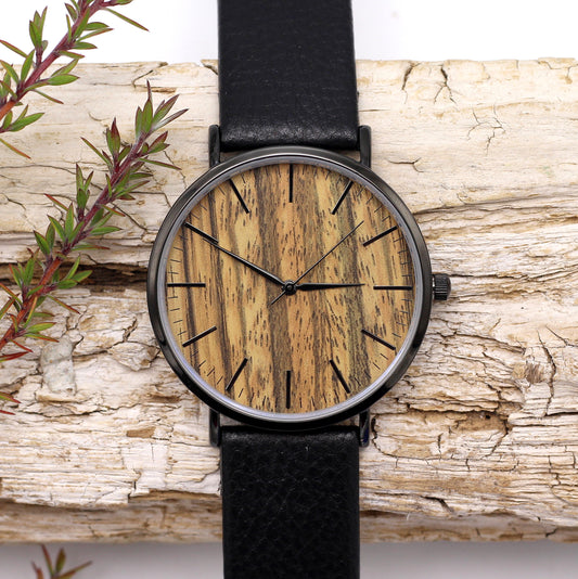A sleek black stainless steel and wood watch with a leather strap displayed on a wooden surface.
